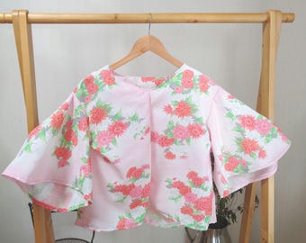 May include: A pink blouse with a floral print featuring pink and white flowers. The blouse has a round neckline and short, wide sleeves.