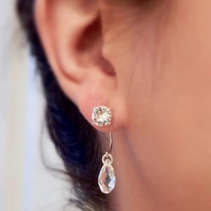 May include: A pair of silver earrings with clear crystal stones. The earrings are a stud and a dangle style.