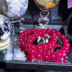May include: A close-up of a pink gemstone bracelet with large, round beads. The bracelet is displayed on a glass shelf with other decorative items.