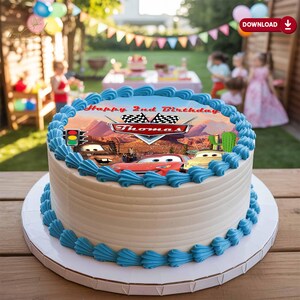 May include: A round birthday cake with white frosting and blue frosting accents. The top of the cake features a Cars-themed image with the text "Happy 2nd Birthday Thomas". The cake is on a white cake board.