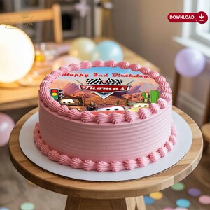 May include: A pink frosted birthday cake with a Cars theme. The cake features an edible image with the text "Happy 2nd Birthday Thomas" and images of the Cars characters. The cake is on a wooden table.