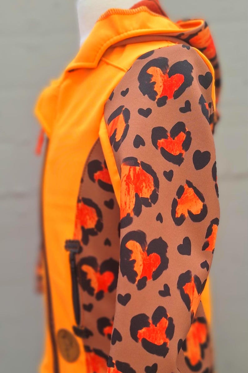 May include: Orange jacket with a brown and orange leopard print on the sleeves. The jacket has a zipper closure and a hood.
