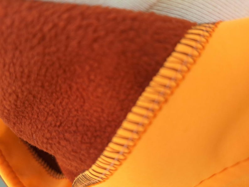 May include: Close-up of a brown fleece lining sewn to a bright orange fabric. The seam is visible and the fabric is textured.
