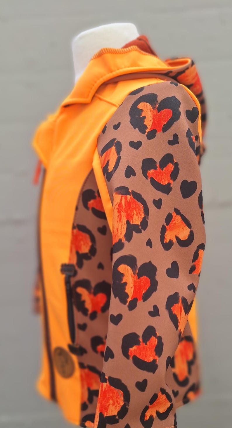 May include: Orange and brown jacket with a leopard print pattern on the sleeves. The jacket has a zip fastening and a hood.