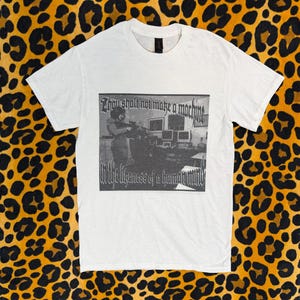 May include: White t-shirt with a black and white graphic print. The graphic features a person holding a weapon in front of computer monitors, with the text "Thou shalt not make a machine" and "in the likeness of a human mind."