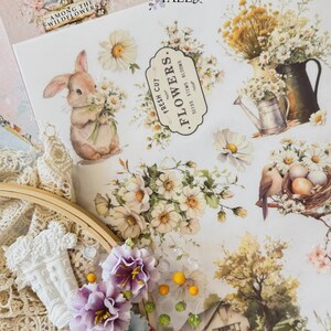 May include: A collage of floral and nature-themed scrapbook elements. Includes a bunny holding flowers, floral arrangements, a birdhouse, and the text "AMONG THE WILDFLOWERS". The color palette is soft with whites, creams, and pastel hues.