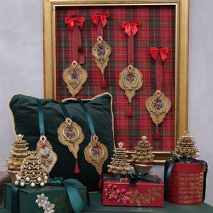 May include: Christmas-themed display featuring ornate ornaments, decorative gift boxes, and miniature Christmas trees. The ornaments have floral designs and red accents. The gift boxes are green and red, adorned with ribbons and floral embellishments. The trees are gold and pearl.