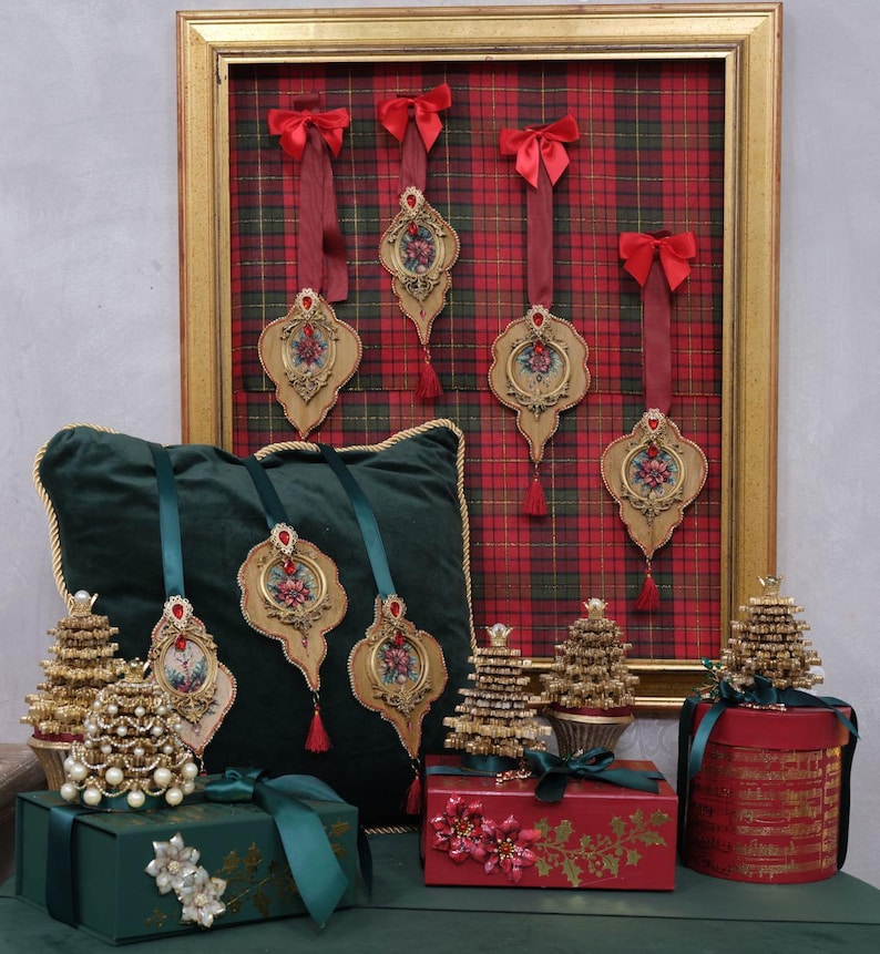 May include: Christmas-themed display featuring ornate ornaments, decorative gift boxes, and miniature Christmas trees. The ornaments have floral designs and red accents. The gift boxes are green and red, adorned with ribbons and floral embellishments. The trees are gold and pearl.