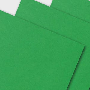 May include: A close-up shot of several sheets of bright green paper, slightly overlapping. The paper has a textured surface and a vibrant, solid color. The arrangement suggests stationery or craft supplies.