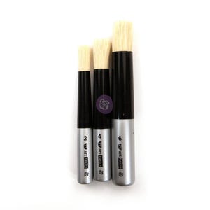 May include: Three paint brushes with light-colored bristles, black ferrules, and silver handles. Each handle is printed with the text "art basics" and a number: 2, 4, or 6. The brushes are arranged vertically in ascending order of size.