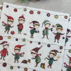 May include: White paper napkins with a festive Christmas elf design. Each napkin features multiple illustrations of elves wearing red and green outfits, holding ornaments and gifts, and strung with colorful lights.