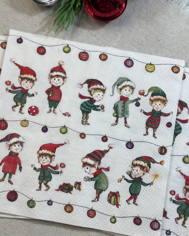 May include: White paper napkins with a festive Christmas elf design. Each napkin features multiple illustrations of elves wearing red and green outfits, holding ornaments and gifts, and strung with colorful lights.