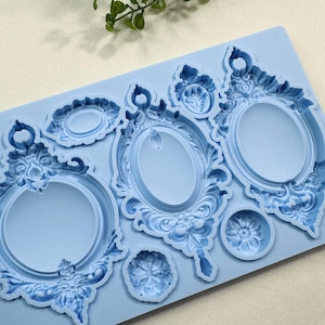 May include: A light blue silicone mold featuring various ornate oval picture frame designs and floral accents. The mold includes several different sizes and shapes, perfect for crafting projects.