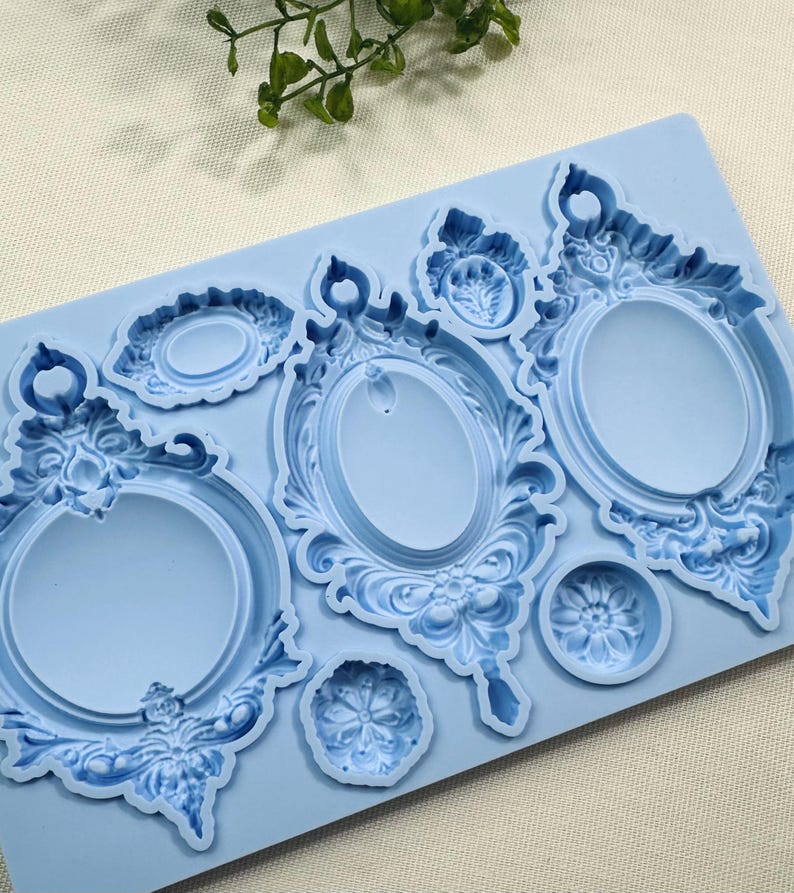 May include: A light blue silicone mold featuring various ornate oval picture frame designs and floral accents. The mold includes several different sizes and shapes, perfect for crafting projects.