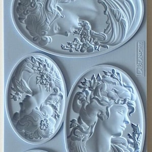May include: A light blue rectangular silicone mold featuring four recessed oval designs. The designs include two detailed profiles of faces surrounded by floral elements, a smaller oval with a single rose, and a larger oval with a face and hair.