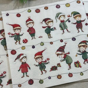 May include: White paper napkins with a repeating pattern of cartoon elves in red and green outfits, wearing hats and scarves. The elves are surrounded by colorful Christmas lights and ornaments.