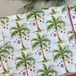 May include: White paper napkins featuring a repeating pattern of green palm trees adorned with colourful baubles. The napkins have a magenta border, perfect for a tropical Christmas celebration.