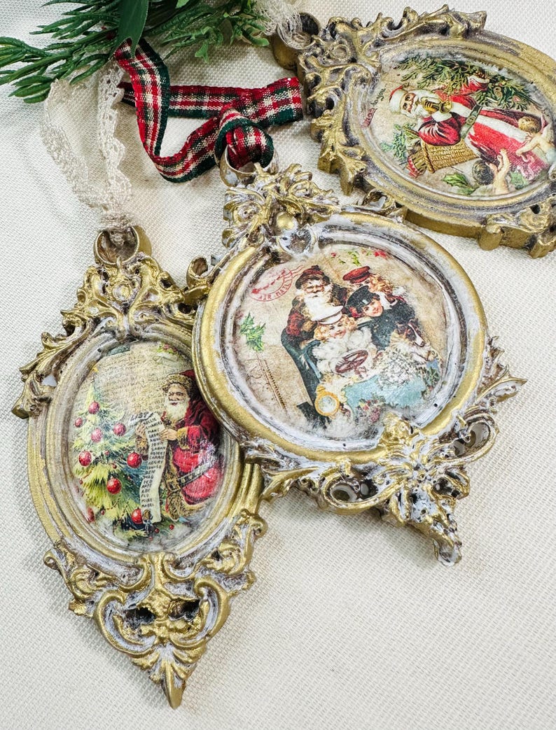May include: Ornate, gold-colored Christmas ornaments with vintage-style Santa Claus illustrations. Each ornament has a unique shape and is accented with white paint. A red and green plaid ribbon and lace are visible.