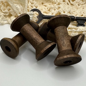May include: Four wooden spools in a dark brown color. The spools are stacked on top of each other.