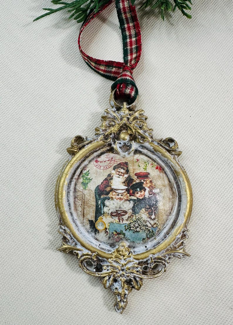 May include: Ornate Christmas ornament with a vintage-style image of Santa Claus and children. The oval-shaped ornament has a gold and white distressed finish, with a red, green, and white plaid ribbon for hanging.