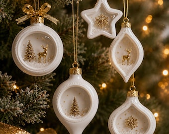 Op de afbeelding: Een set van vijf witte keramische kerstornamenten met gouden accenten. De ornamenten bevatten interne diorama's met gouden herten, dennenbomen en sneeuwvlokken op een besneeuwde ondergrond. Elk stuk is voorzien van een gouden dop en een koordje.