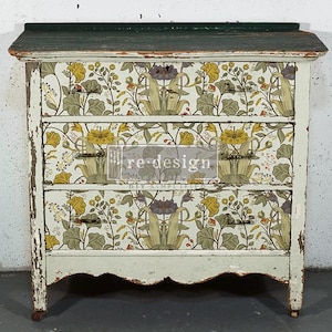 May include: A wooden chest of drawers with a distressed light green finish and a dark green top. The three drawer fronts feature a floral pattern in yellow, green, and purple tones. A rectangular logo with the text re-design is visible.