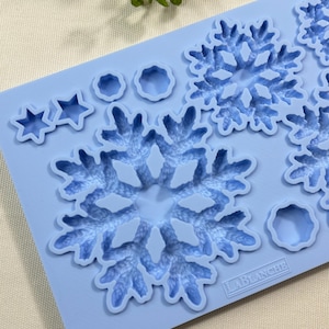 May include: A light blue silicone mold featuring various winter-themed shapes. The mold includes snowflake designs, star shapes, and circular patterns. The brand name "LABLANCHE" is printed on the mold. Ideal for crafting and baking.