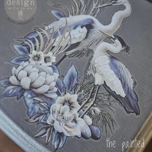May include: Decorative transfer featuring two herons with blue and white feathers, surrounded by white flowers and blue leaves. The design is on a grey background with the text "the painted UNICORN".
