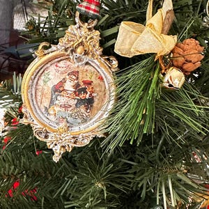 May include: Ornate gold-colored Christmas ornament with a vintage image of a family. The ornament is round with a decorative frame and a red and green plaid ribbon for hanging. The ornament is displayed on a green Christmas tree.