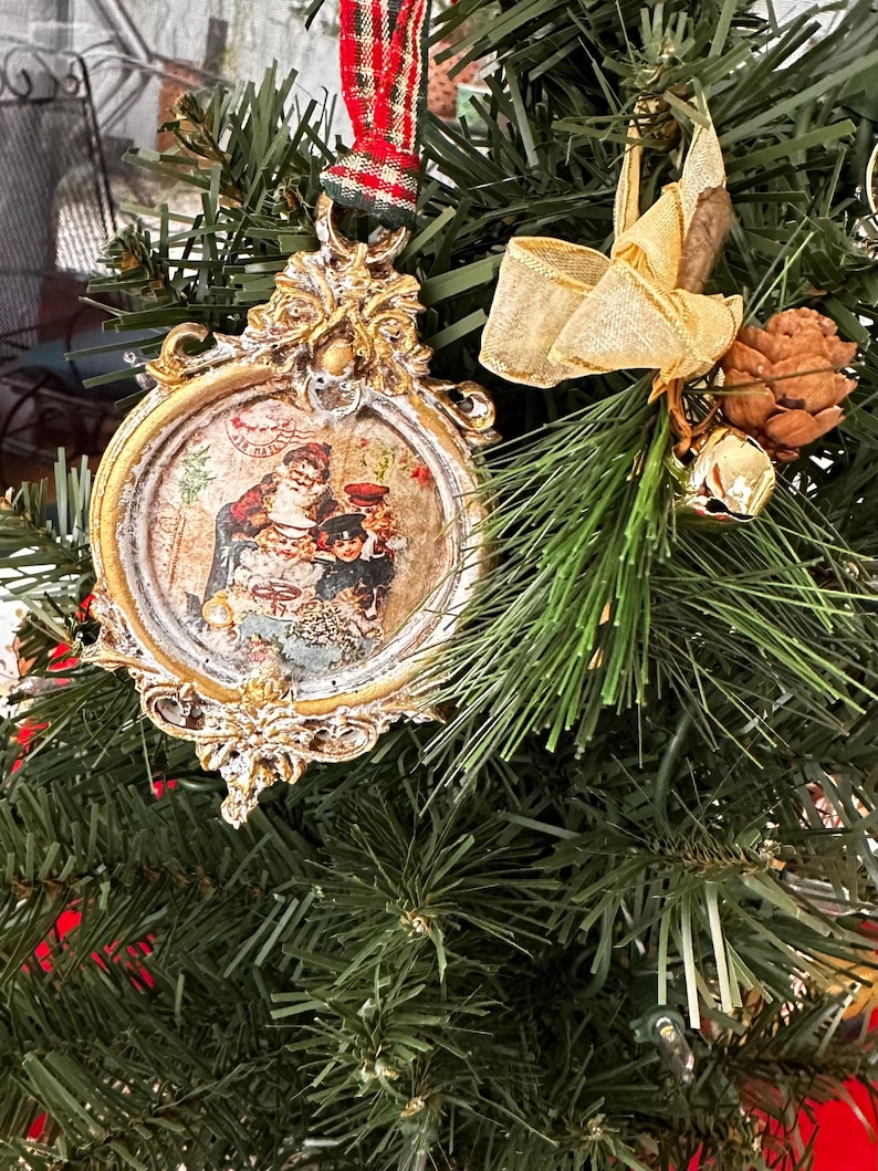 May include: Ornate gold-colored Christmas ornament with a vintage image of a family. The ornament is round with a decorative frame and a red and green plaid ribbon for hanging. The ornament is displayed on a green Christmas tree.