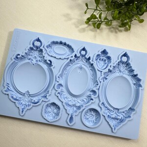 May include: A light blue silicone mold featuring several ornate, vintage-style picture frame designs. The mold includes oval and round frames with detailed scrollwork and decorative elements, perfect for crafting projects.