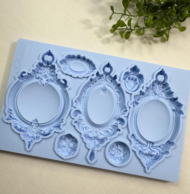May include: A light blue silicone mold featuring several ornate, vintage-style picture frame designs. The mold includes oval and round frames with detailed scrollwork and decorative elements, perfect for crafting projects.