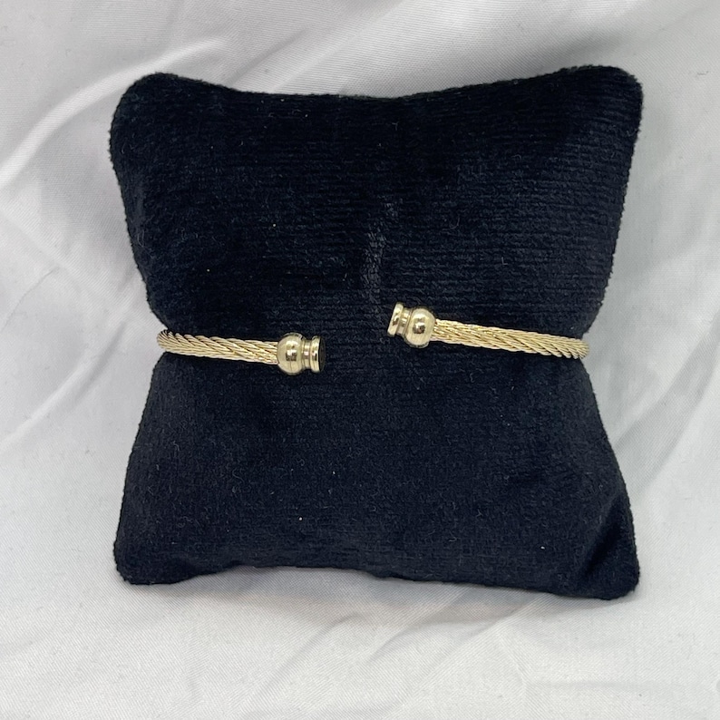 May include: A gold-toned bangle bracelet with a twisted cable design and rounded ends.