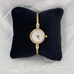 May include: A gold-toned wristwatch with a white face and a cable-style band.