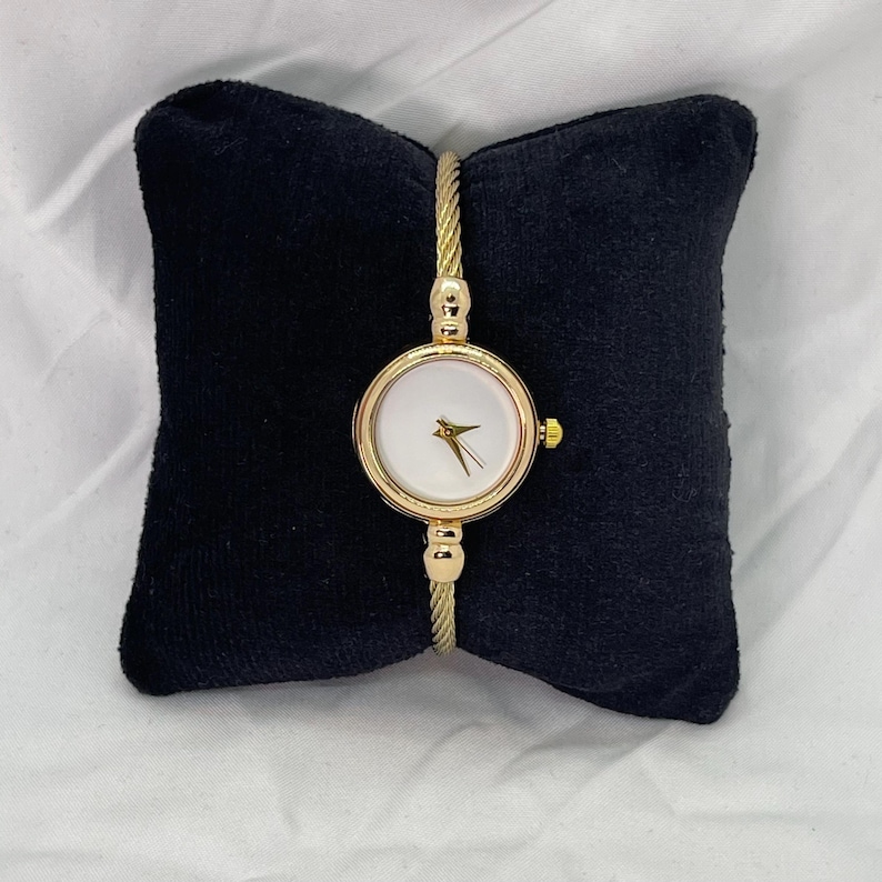 May include: A gold-toned wristwatch with a white face and a cable-style band.