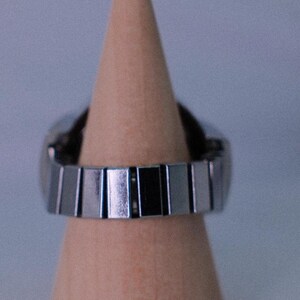 May include: A silver metal watch band with a polished finish. The band is on a wooden display stand.