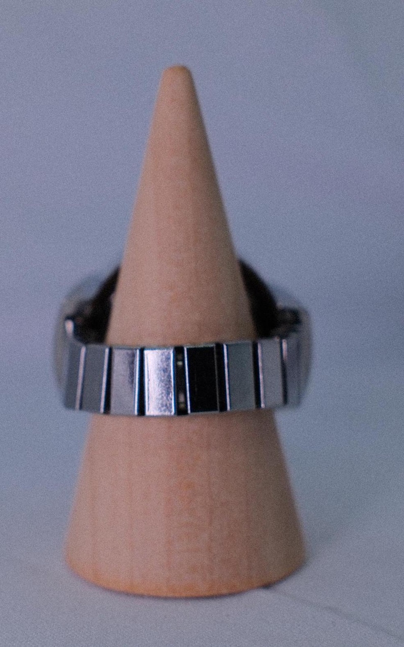 May include: A silver metal watch band with a polished finish. The band is on a wooden display stand.