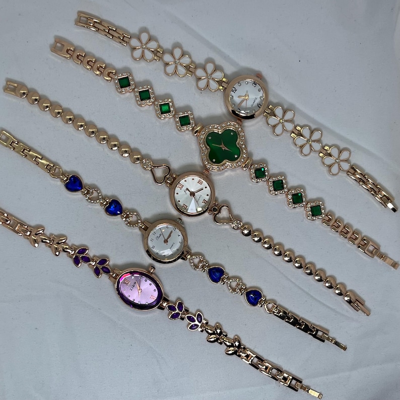 May include: Five gold-tone wristwatches with different colored crystal accents and face designs. The watches have a variety of band styles, including a chain link, a beaded, and a leaf design.