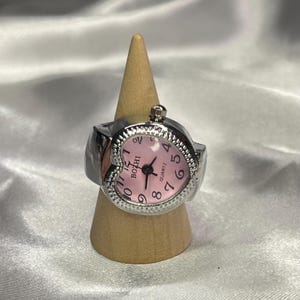 May include: A silver heart-shaped ring watch with a pink face and black numbers. The watch face says "BOZHI QUARTZ".