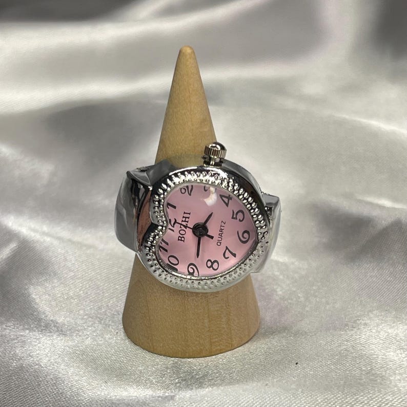 May include: A silver heart-shaped ring watch with a pink face and black numbers. The watch face says "BOZHI QUARTZ".