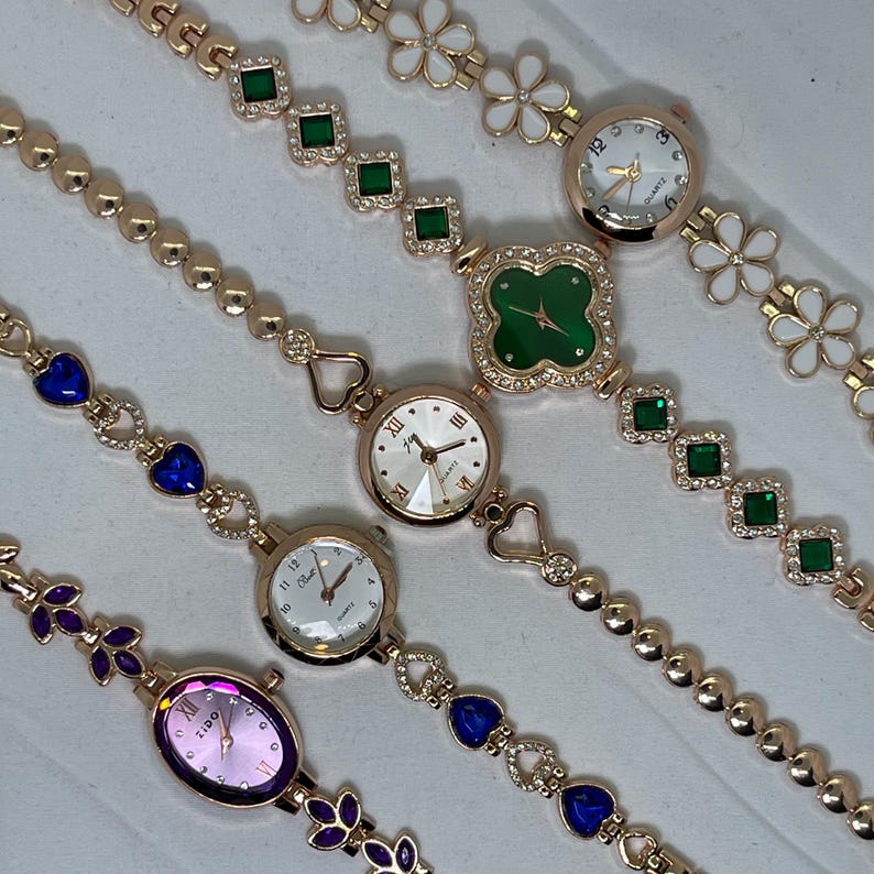 May include: Four gold-tone wristwatches with different colored face designs and jeweled bands. The bands feature different patterns, including hearts, flowers, and squares.