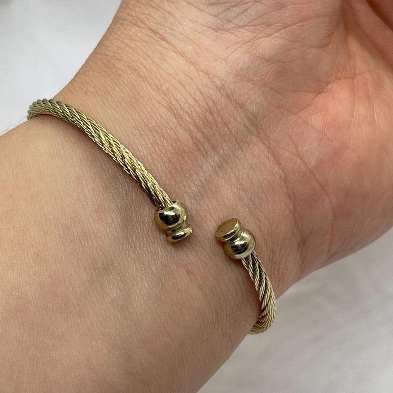 May include: A gold-toned cable bracelet with two round, smooth, ball-shaped clasps.