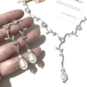 Op de afbeelding: Zilveren ketting- en oorsteensets met een delicaat rankontwerp en glinsterende heldere stenen. Elk stuk is versierd met een parel-druppel.