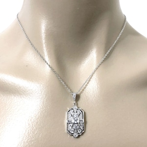 Puede incluir: Un collar de tono plateado con un colgante rectangular de dise&ntilde;o geom&eacute;trico. El colgante est&aacute; engastado con m&uacute;ltiples piedras transparentes facetadas, incluida una piedra central cuadrada rodeada de piedras redondas y de corte baguette.