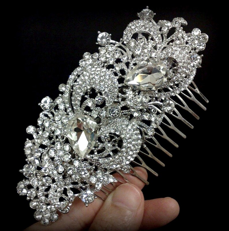 May include: Silver hair comb with a large, ornate design featuring clear rhinestones and two large teardrop-shaped crystals.