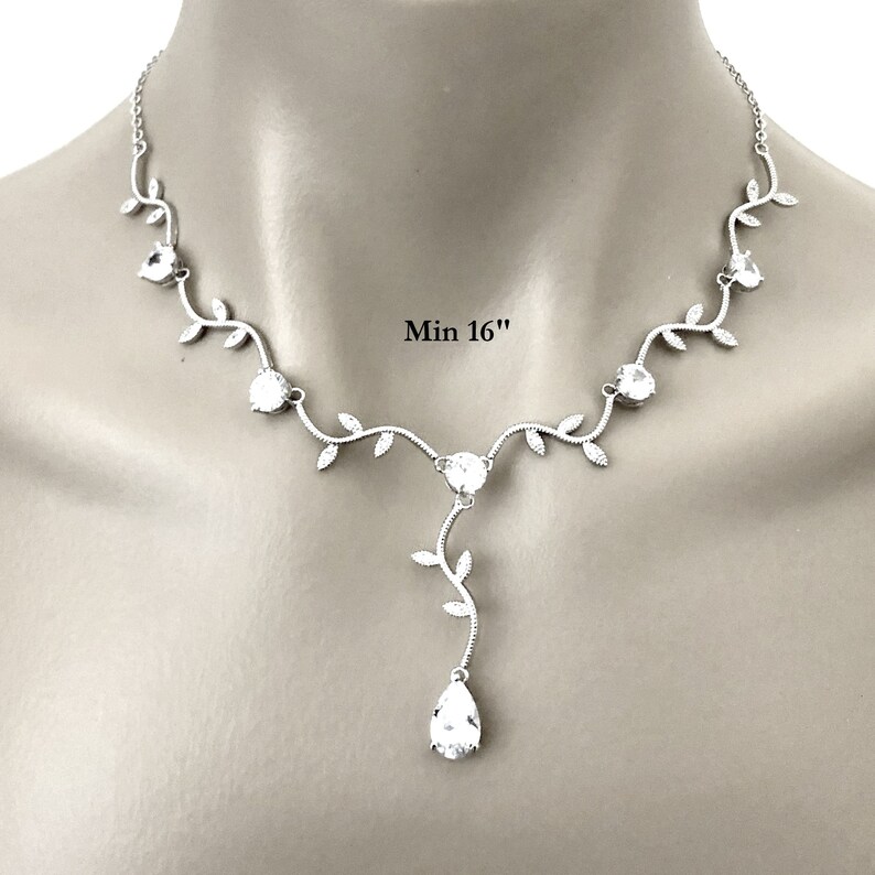 Op de afbeelding: Zilveren ketting met een delicaat rankontwerp en heldere kristallen. De ketting heeft een druppelhanger met een peervormig kristal. Min 16"