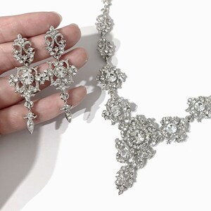 May include: A silver necklace and earrings set with a delicate floral design and clear rhinestones.