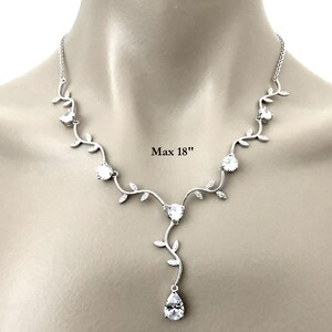 Op de afbeelding: Een zilveren ketting met een delicaat rankontwerp en heldere kristallen. De ketting heeft een hangende hanger met een peervormig kristal. Max 18" lang.