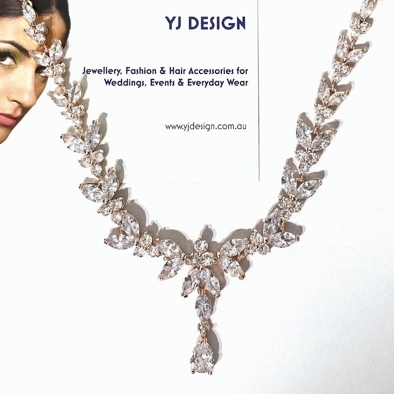 May include: Rose gold-toned necklace and headpiece with clear, sparkling crystal accents. The jewelry features a leaf-like design and a teardrop pendant. The image includes the text "YJ DESIGN" and "Jewellery, Fashion & Hair Accessories for Weddings, Events & Everyday Wear."