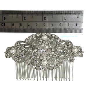 May include: Silver hair comb with a large, ornate design featuring clear rhinestones and faux pearls. The comb is approximately 4 inches wide.